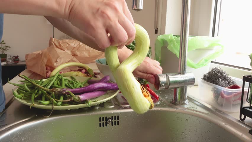 Woman wash vegetables zucchini under running water in kitchen. Healthy food and vegetables. Organic seasonal farm products.