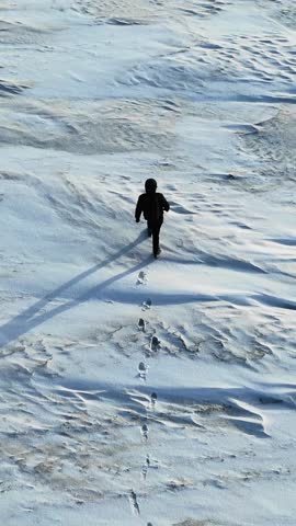 A lonely human walk by snow desert. Footprints on the snowy field. A person walks alone through a pristine snow desert, viewed from above in FHD quality.