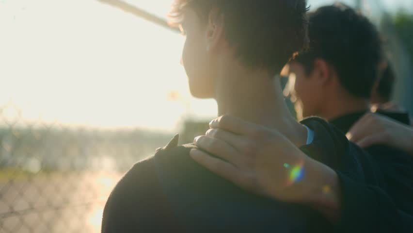 A close-up shot of three teenage boys with arms around each other is shoulders, bonding as friends. The sunlight and relaxed vibe highlight their strong connection.
