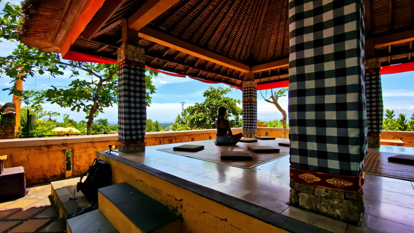 Person meditating in a traditional gazebo with scenic Bali views in the background