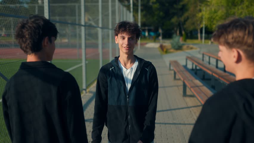 Teen boys hug and smile by the school is sports area. A big show of brotherhood, joy, and team spirit captured in a real, heartfelt moment.
