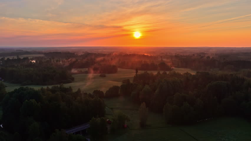 Aerial of vibrant orange sunrise sunset over misty landscape and treetops in the distance