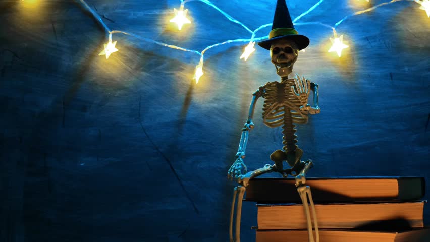 Spooky Halloween Stories.Skeleton sitting on book and garlands in blue color on chalkboard background.Halloween books. 4k footage
