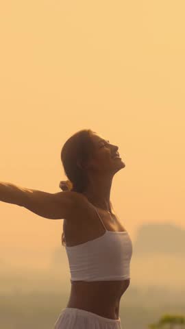 Slow motion vertical video of a woman in a white outfit opening her arms at sunrise with a smile. Uplifting, serene nature scene perfect for social media, wellness, and lifestyle branding.