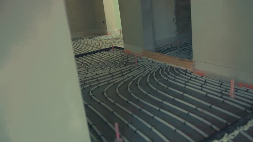 Construction workers installing underfloor heating system pipes in new apartment
