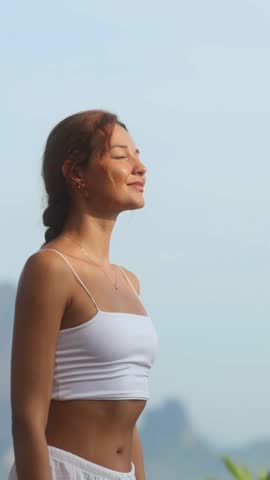 Slow motion vertical shot of a happy woman stretching arms wide under a clear blue sky in a natural setting. Perfect for lifestyle, wellness, freedom, and personal growth content or ads.