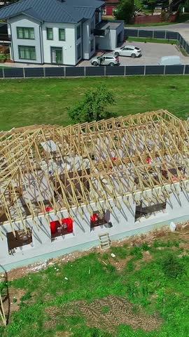Wooden roof framing and trusses of a new residential house being built in the Latvian countryside, showing the home construction process - Aerial vertical parallax