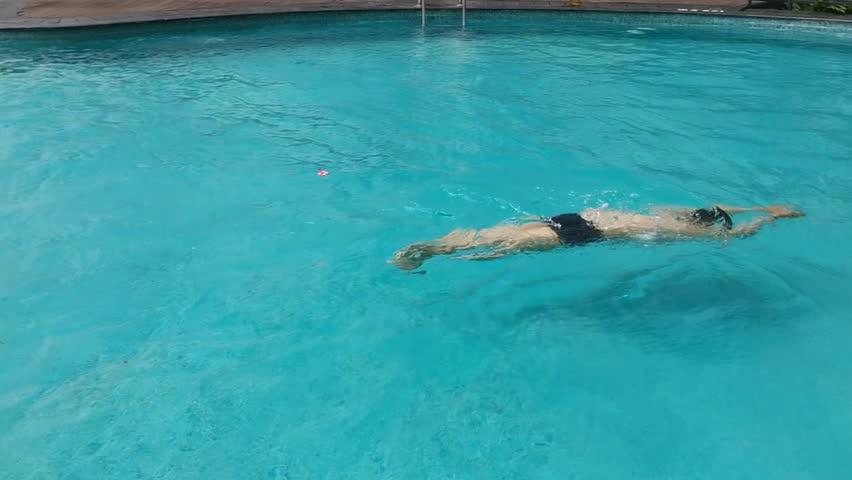A sequence showcasing a person proficiently executing the freestyle swimming stroke in a serene outdoor pool setting. The video highlights the rhythmic movements, emphasizing the balance.