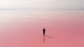 Surreal drone footage of solo traveler walking across reflective pink lake with backpack. High quality conceptual travel or exploration promo with minimalist landscape and vivid colors. - Powered by Shutterstock - Get 15% off with code: PIKWIZARD15