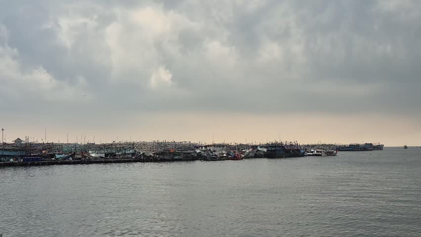 A fleet of fishing boats docked under overcast skies—capturing the calm before the storm in a coastal village, with moody weather and a tranquil maritime atmosphere.