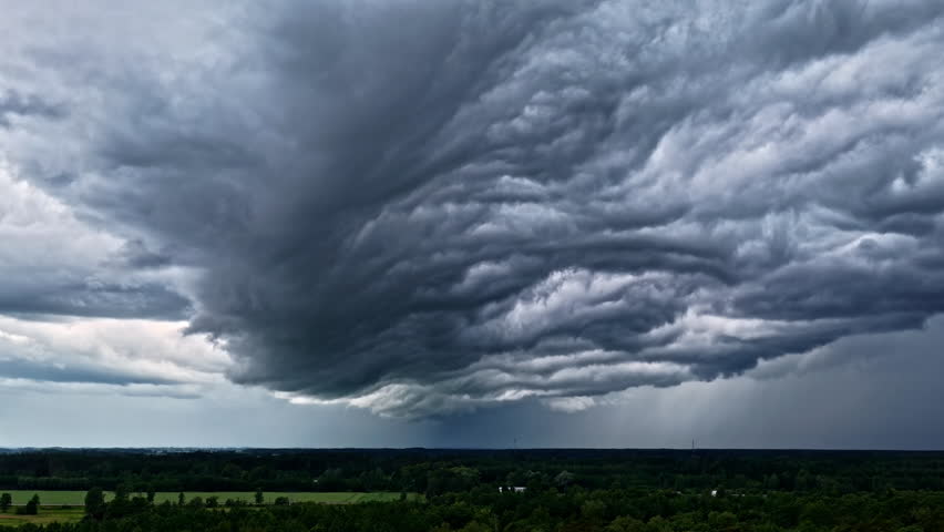 Massive storm cloud system stretches over open green field under dark sky before rainfall begins, twister background