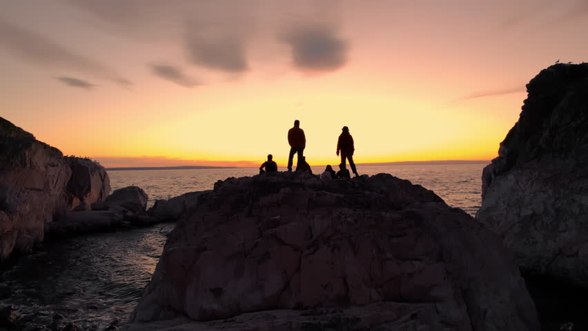 Group of diverse tourists sitting and standing on a rock on the shore of a lake enjoying rest and watching sunset scenery after a day of hiking. Joy of reaching a goal. Gobi Desert in Mongolia.