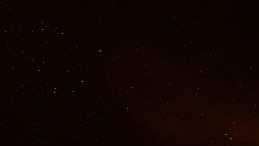 Flying glowing fire sparks in darkness, isolated particles of burning embers on black background, 4K slow motion with selective focus