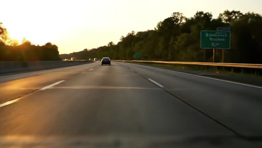 Real-time dashcam perspective of highway driving in the U.S., with authentic textures, shadows, and road signs. Footage includes a distant vehicle ahead. Clean composition without any branding or peop