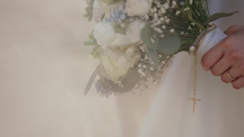 bride holding white bouquet with golden cross pendant and wedding ring visible