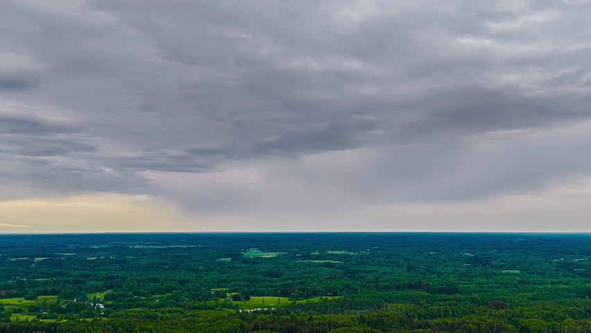 Time lapse of dark storm clouds moving over green farmland landscape, natural backdrop of storm grey clouds