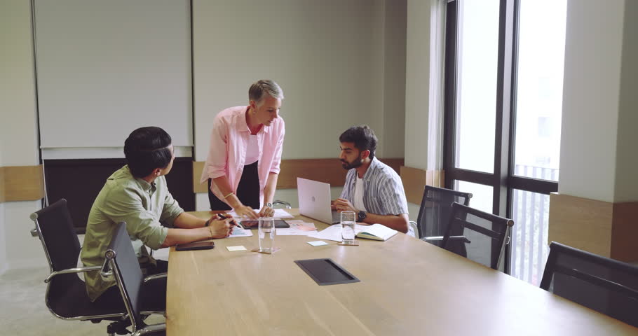 Diverse coworkers responding to data briefing by leaning over conference table discussing charts. Collaboration, teamwork, analytics, meeting, office, strategy, communication