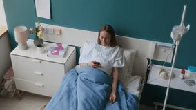 Medium full high-angle shot of pregnant young woman in white rove lying in bed in maternity clinic while receiving intravenous infusion, putting down gadget and looking out of window - Powered by Shutterstock - Get 15% off with code: PIKWIZARD15