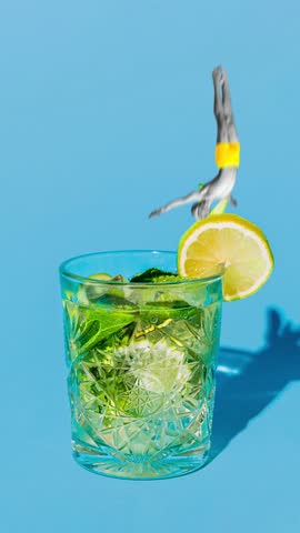 Creative video ad. Legs in mid-dive emerge from refreshing glass of Mojito, with slice of lemon perched on rim. Concept of summer, holidays, celebration, Friday mood, festivals.