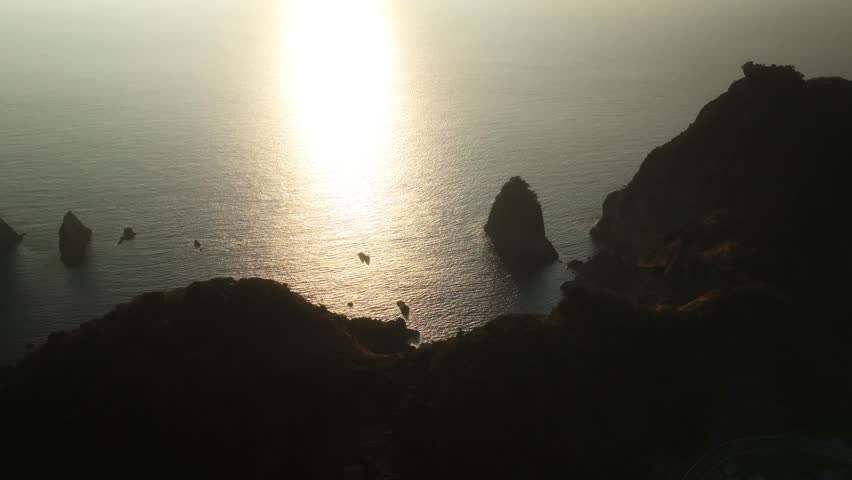 Aerial view of the rugged Kumomi Shore coastline with a small village nestled at the base of the cliffs, creating a striking contrast, Kumomi Shore, Shizuoka, Japan.