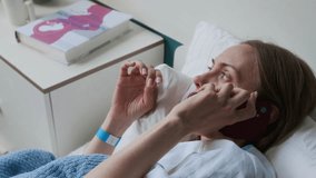 Close-up of anxious pregnant young Caucasian woman lying on pillows in bed at maternity clinic, having conversation on mobile phone with husband or family, fidgeting fingers - Powered by Shutterstock - Get 15% off with code: PIKWIZARD15