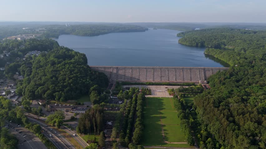 Traffic scene on interstate road near Kensico reservoir plaza dam in New York. Aerial wide shot. Cars on road in suburb of town.