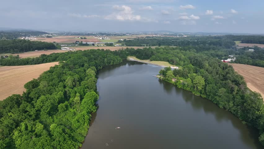Lake in idyllic landscape of America. Farmsteads and homes surrounded by colored cultivated farm fields. Aerial flyover shot . Dam barrier at shoreline. Beautiful nature of America.
