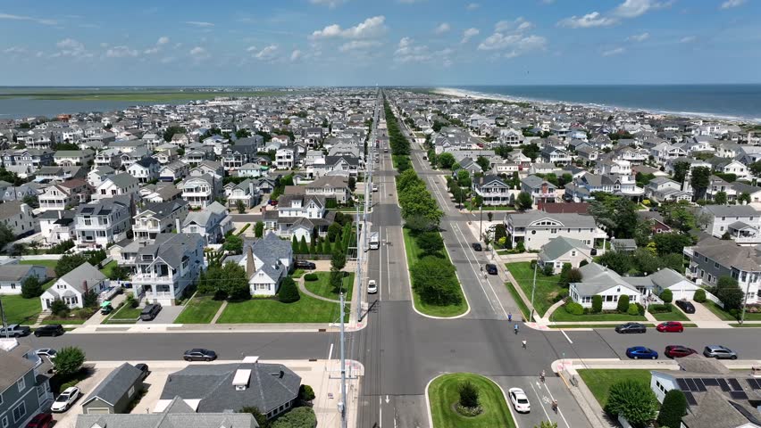 Stone Harbor, New Jersey. Luxury beach houses with solar panels, tree-lined roads, Atlantic Ocean and classic American coastal town symmetry under blue summer sky. Aerial wide shot.