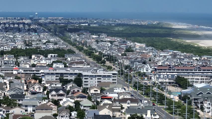 Main Street leading to stone harbor beach in New Jersey. Sunny day with blue Atlantic Ocean in distance. Aerial panorama wide shot. Traffic scene in American coastal town of USA.