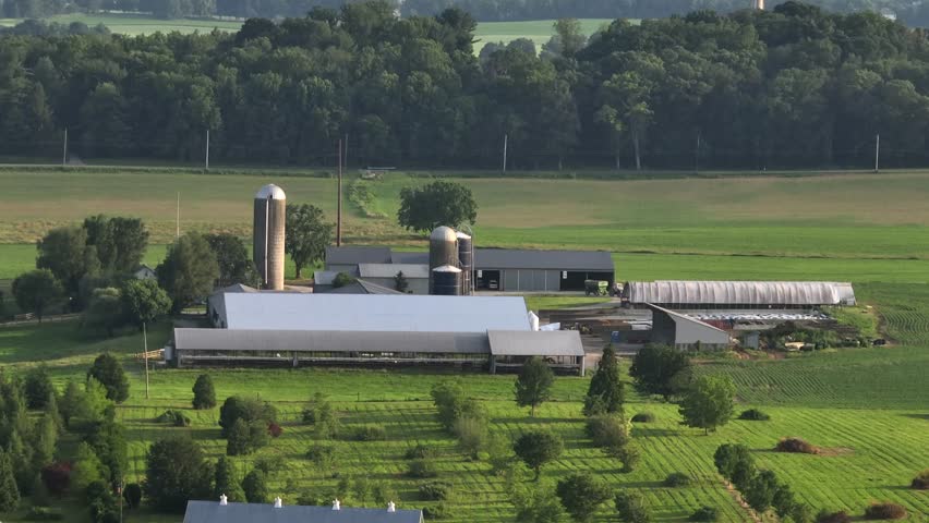 American property in rural district of town. Farmstead with barns and chicken house during sunset time in summer. Aerial zoom shot.
