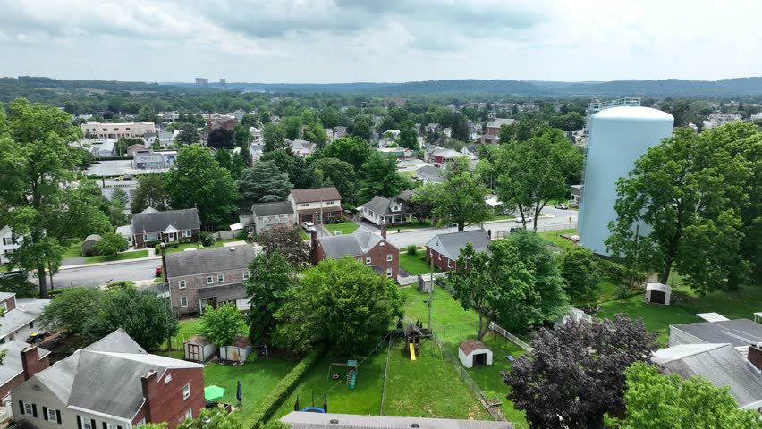 Drone flight over American town named Middletown, PA in summer. Water tower in center of small neighborhood. Aerial Birds Eye shot. Cloudy day with green yards.