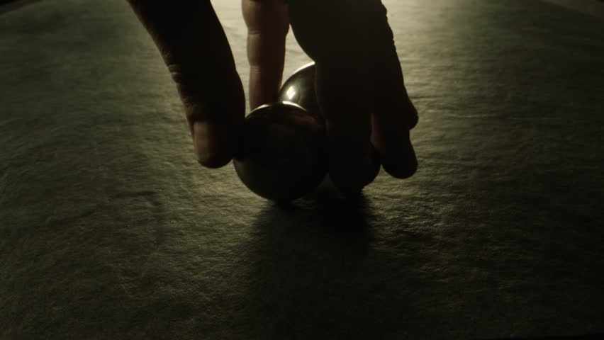 Three silicon nitride balls are rolling on the ceramic floor . Big medium and small heavy metallic or ceramic balls moving , knocking , hitting each other on dark room in concrete surface slow motion