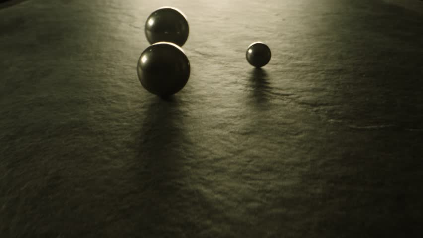 Three silicon nitride balls are rolling on the ceramic floor . Big medium and small heavy metallic or ceramic balls moving , knocking , hitting each other on dark room in concrete surface slow motion