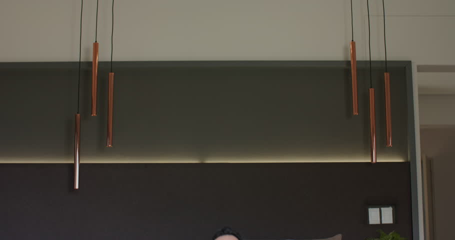 Senior Asian man unrolling black yoga mat and meditating in bedroom under copper pendant lights. Mindfulness, relaxation, serenity, wellness, interior, tranquil, contemplation