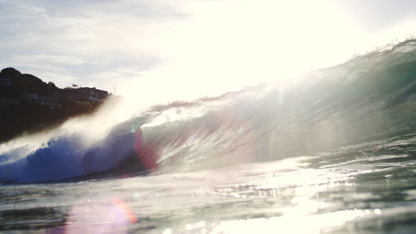 Cinematic flare and sunlight beam over rolling wave lip in artistic telephoto slow motion