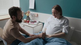 Medium full zoom shot of pregnant Caucasian woman sitting in bed in maternity clinic, experiencing painful contractions, screaming in pain, nurse giving oxytocin drip, husband holding wife by hand - Powered by Shutterstock - Get 15% off with code: PIKWIZARD15