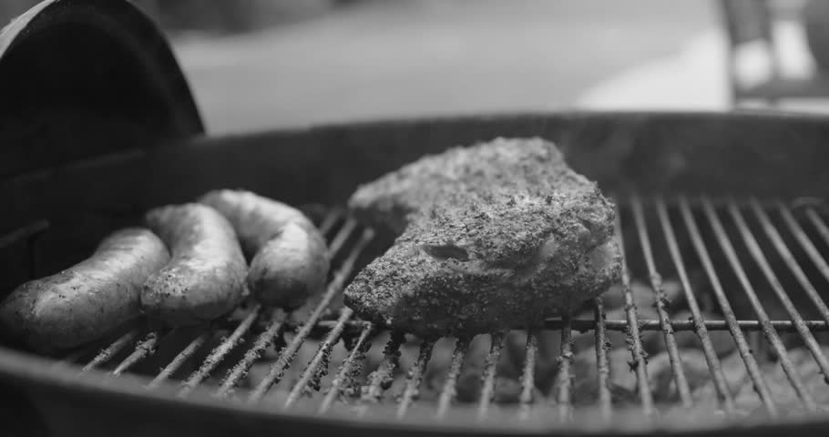 A black and white close-up shows sausages and a large, seasoned cut of meat smoking on a grill, with visible wisps of smoke.