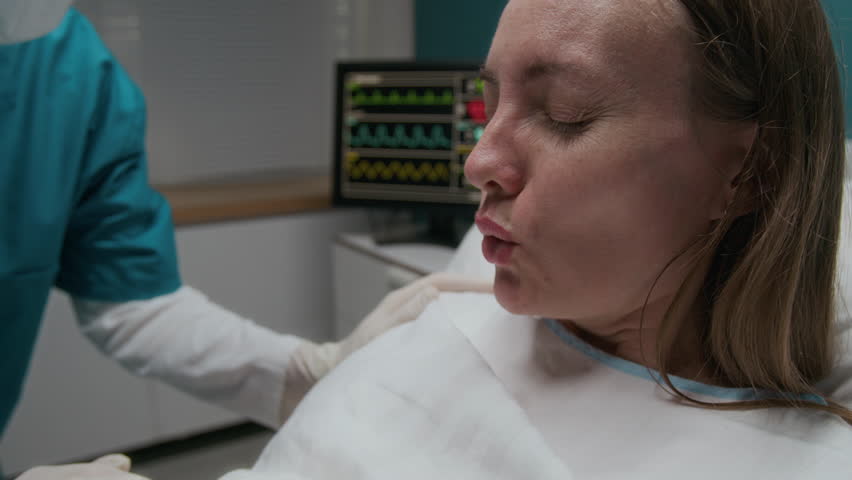 Handheld medium close-up of face of sweaty pregnant woman making rhythmic breaths, shouting with pain, pushing during labor, while preparing to deliver baby in maternity hospital