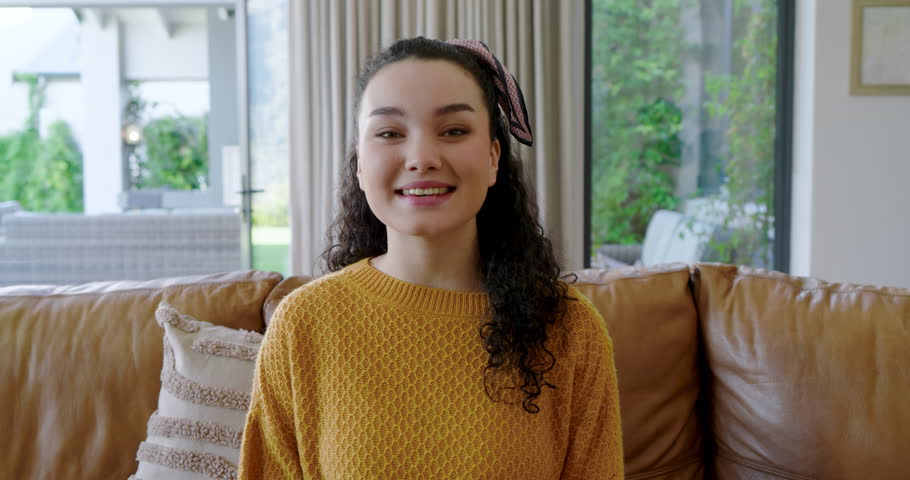 Receiving camera cue, woman in her twenties gesturing and sharing message on leather couch at home. Communication, storytelling, engagement, lifestyle, modern, authentic, expressive