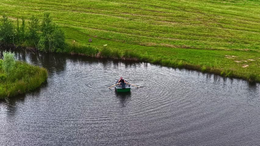 A high-angle aerial shot shows a young couple in a small rowboat enjoying a peaceful and romantic summer day on a calm lake in the Latvian countryside.