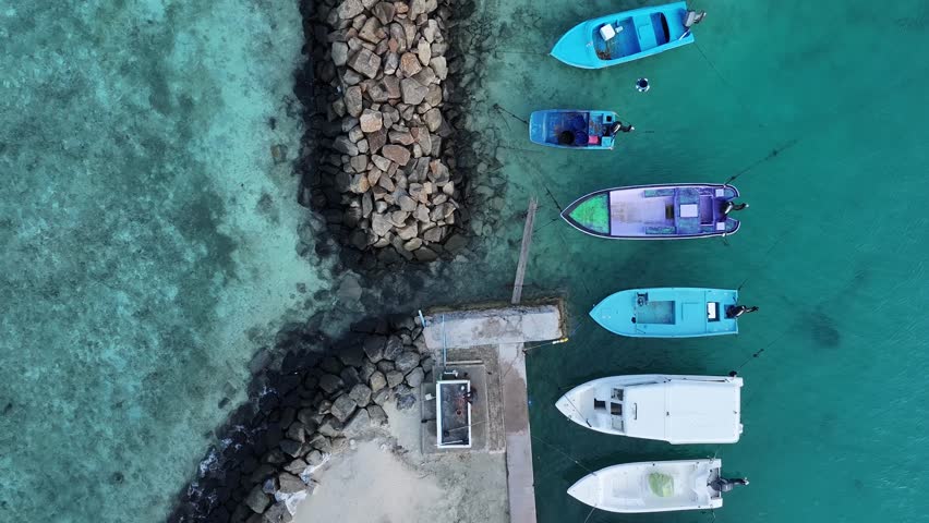 Aerial view of several boats moored near a rocky shoreline, contrasting with the turquoise water in a captivating coastal scene, Gulhi, Kaafu Atoll, Maldives.