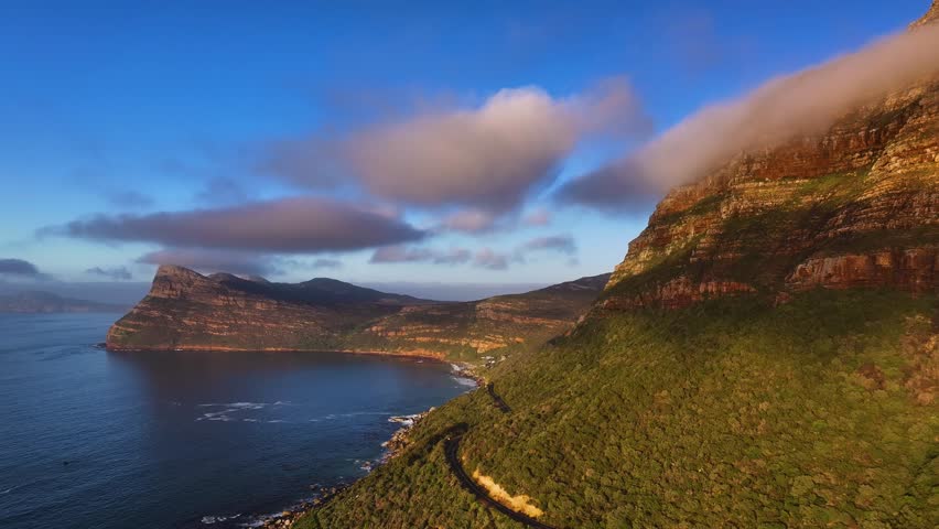 Aerial view of rugged mountains meet the deep blue sea under a partly cloudy sky, creating a stunning contrast of textures and tones, South Africa.