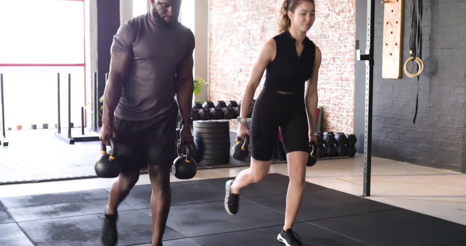 Diverse workout partners starting routine at gym performing alternating lunges with kettlebells. Fitness, strength, stamina, teamwork, resilience, training, wellness