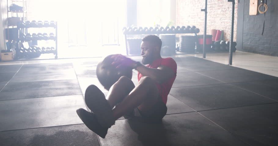 Driven by core strength, African American man twisting torso while holding medicine ball in gym. Fitness, strength, vitality, workout, determination, athleticism, energetic