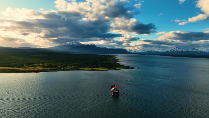 Aerial view of a red and black ship sailing through blue waters, contrasting with the distant snow-capped mountains, Chile.