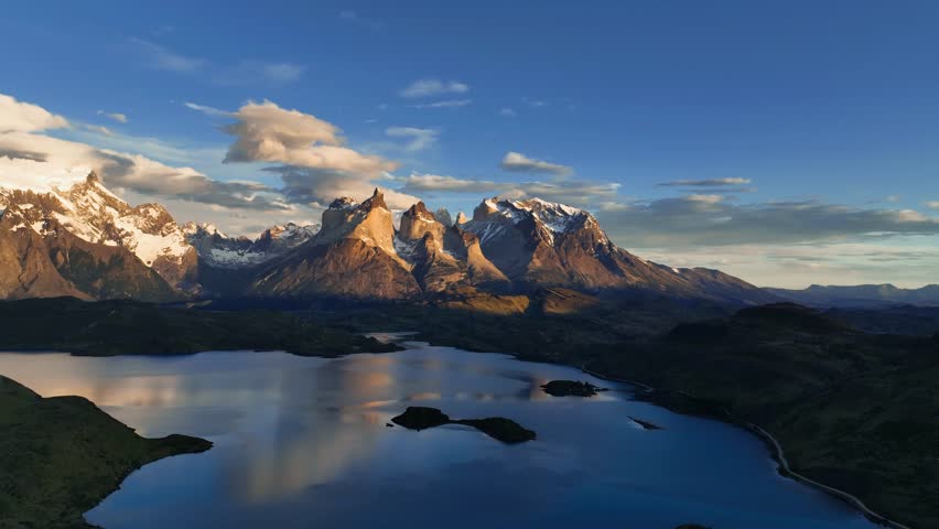 Aerial view of the rugged, snow-capped mountains and shimmering lake in Torres del Paine National Park, a symphony of nature