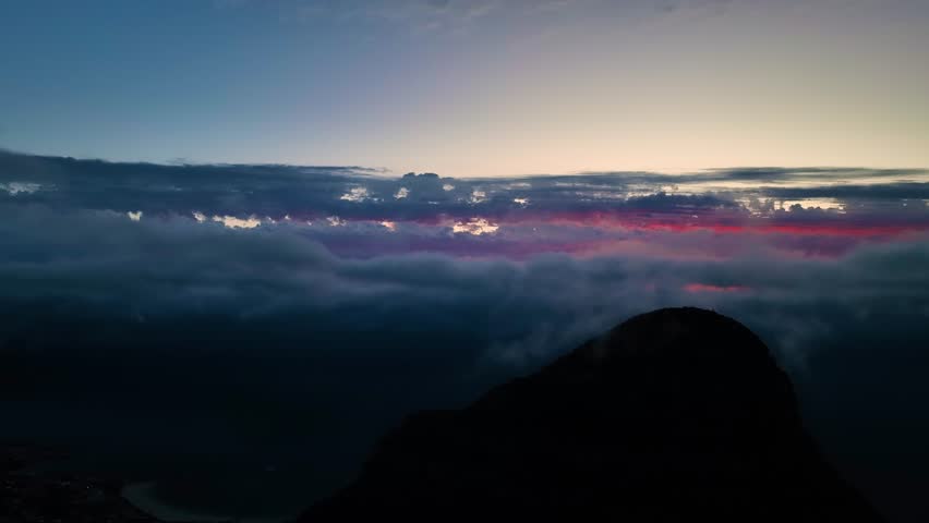 Aerial view of a mountain peak piercing through a sea of clouds with a glowing horizon, creating a dramatic and ethereal landscape, Cape Town, South Africa.