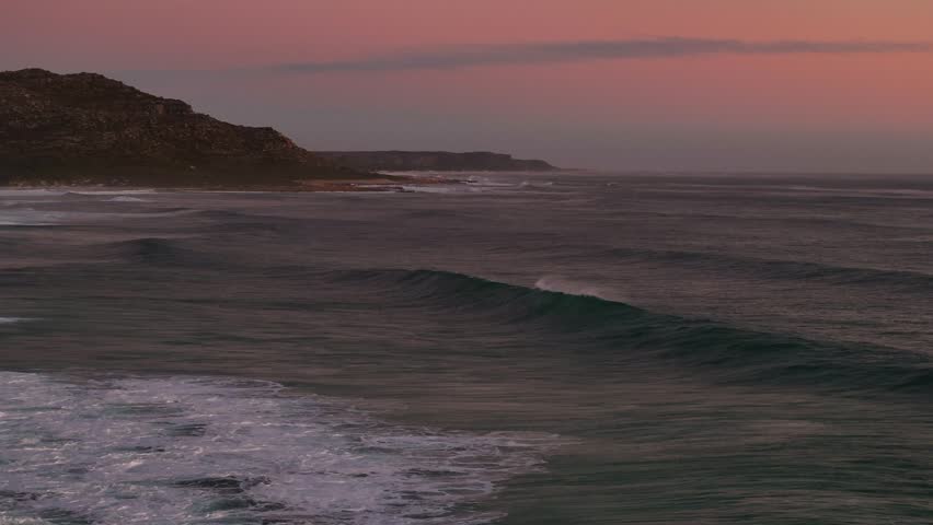 Aerial view of powerful ocean waves crashing against the shore at sunset, a display of nature