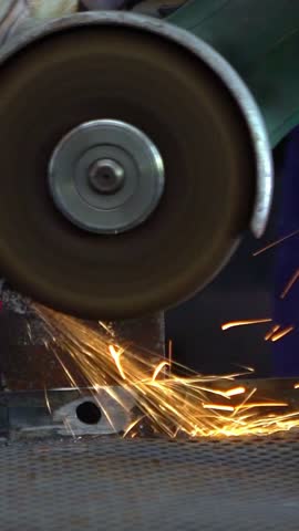 Slowmotion of metal processing with a man using angle grinder to cleaning the steel seam. Locksmith in special clothes and gloves works in production. Sparks in metalworking.