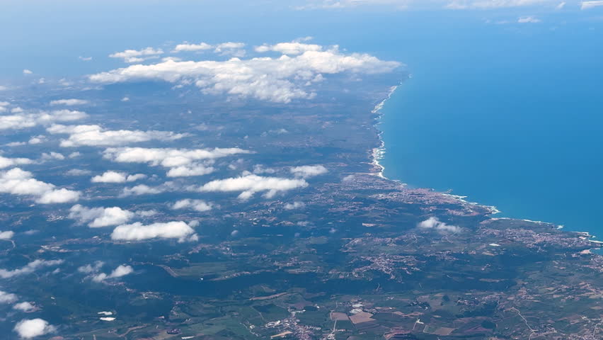 Aerial view of coastline and inland towns under scattered clouds